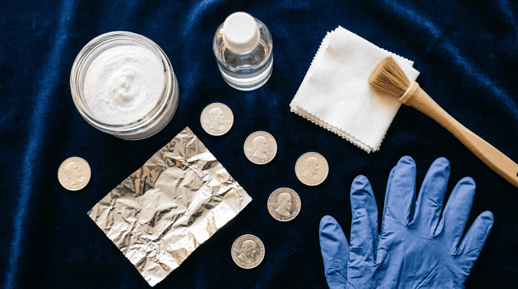 Kit completo para limpiar monedas de plata en casa: bicarbonato, agua destilada, paños de microfibra, guantes de nitrilo y cepillo suave sobre fondo azul.